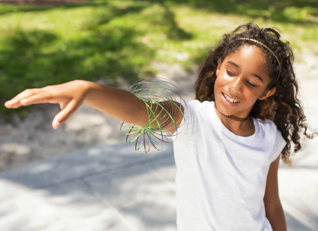 Young girl playing outdoors with the Mozi - Iridescent sensory spring toy spinning on her arm.