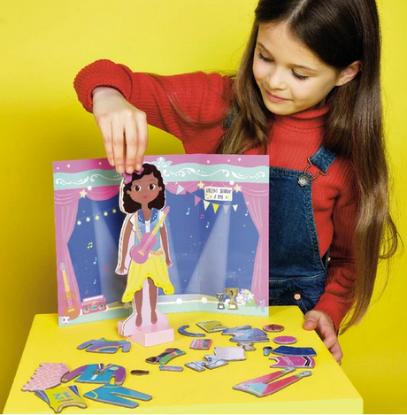 A girl playing with the Magnetic Dress Up | Zoey wooden doll and magnetic outfit pieces on a colorful backdrop.