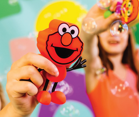 Glo Pals Elmo Character held by child with bubbles in colorful background, playful and friendly toy for kids.
