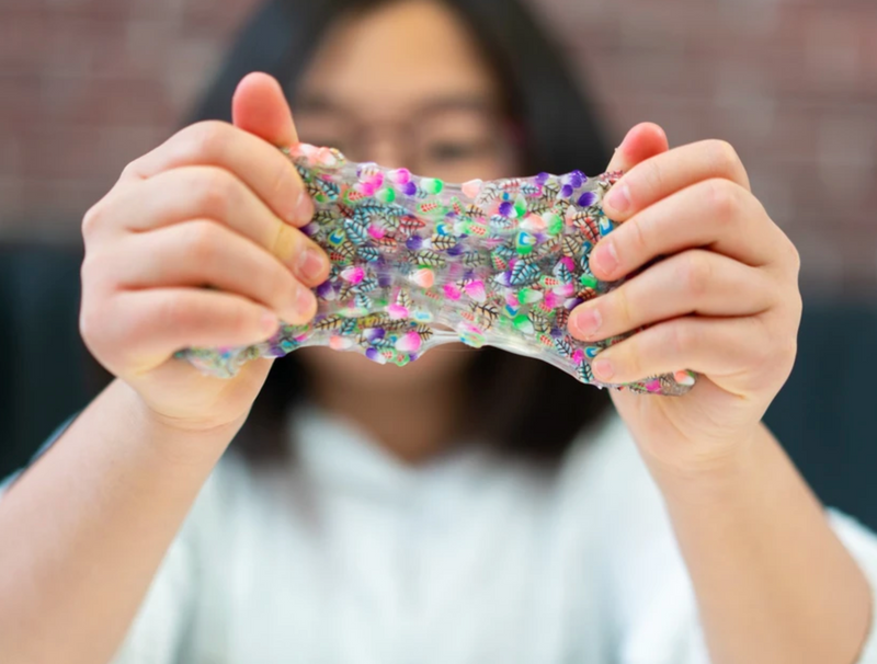 Child stretching colorful Jumbled Jungle Thinking Putty with clay pieces inside clear based silicone putty.