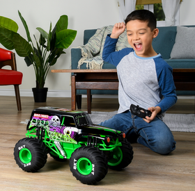 Child playing with a 1:15 scale RC Monster Jam Grave Digger remote control truck indoors on the floor.