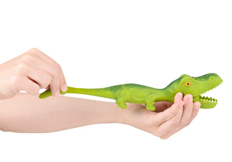 Hand stretching a green squeezy toy alligator showing its stretchy tail, called Stretchy Sand Dino.