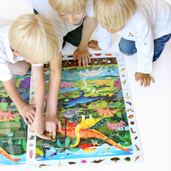 Three children playing and assembling the 60pc Dinosaurs Floor Puzzle with colorful dinosaur illustrations.