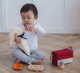 Toddler playing with a stuffed animal and feeding accessories from the Doll Feeding Set for pretend play.