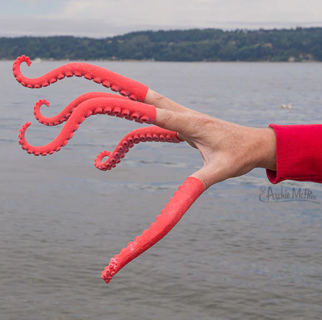 Hand wearing five pink and red Finger Tentacle covers resembling squid tentacles by the water.
