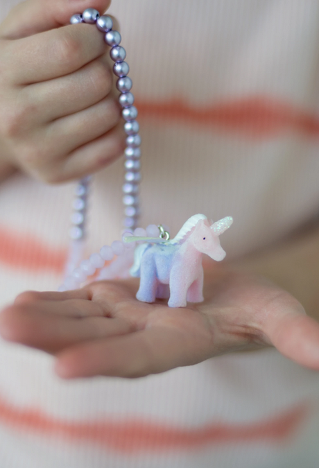 Close-up of a hand holding the Fancy Unicorn Necklace with a pink and purple unicorn pendant and iridescent beads.