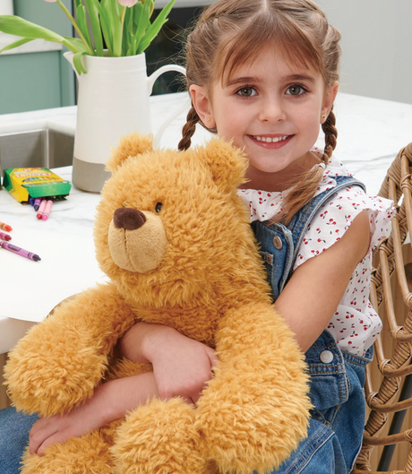 Young girl smiling and hugging a 15” classic brown Teddy Bear Growler plush with soft fur and round paws