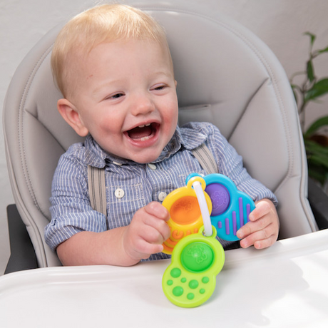 Happy toddler holding colorful Dimpl Clutch with sensory dimpl bubbles and silicone textures on clip ring.