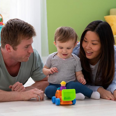 Baby playing with parents and the colorful Press & Go Dump Truck encouraging motor skills and active play.