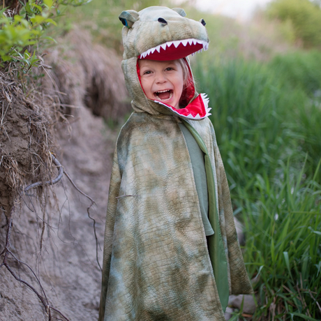 Child wearing the Grandasaurus T Rex Cape with Claws outdoors, smiling with the dinosaur hood and open mouthpiece.