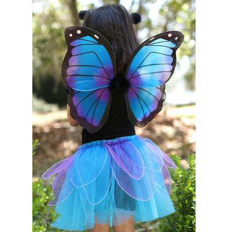 Child wearing the Midnight Butterfly Set with blue glitter skirt, iridescent wings, and butterfly antennae headband outdoors.