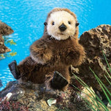 Sea Otter Baby Puppet sitting on a rock by water, featuring soft fur and soulful eyes for interactive play.