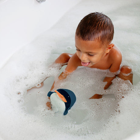 Child playing with CHOMP Hungry Whale bath toy, squeezing tail to open mouth in bubbly bathtub.