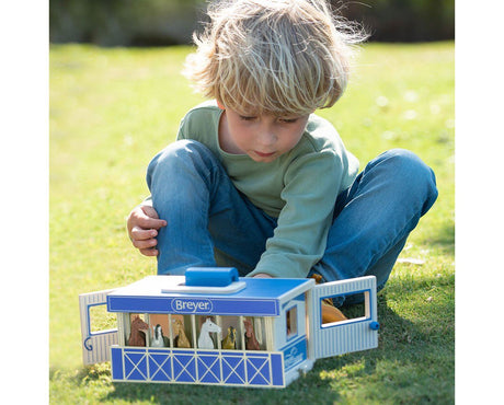 Young child playing outdoors with the Stablemates Wooden Stable Set featuring horses in a blue wooden carry case.