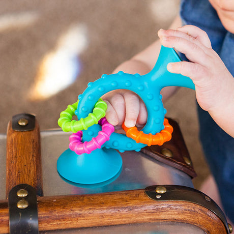 Baby holding and playing with the pipSquigz Teal Loop sensory toy with suction cup and colorful rings.