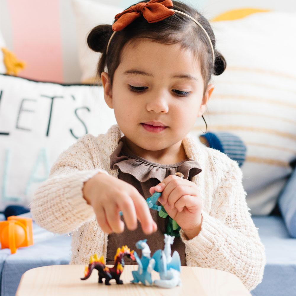 Young girl playing with six dragon figurines from the TOOB | Dragons of the Elements set on a wooden table.