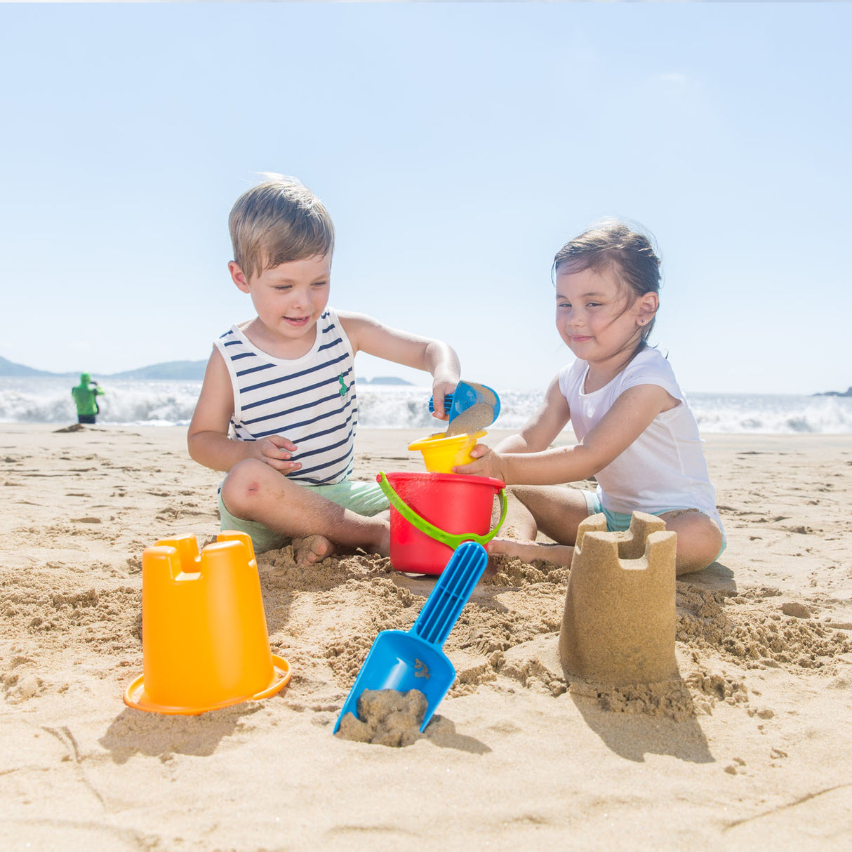 Children playing in the sand using the Beach Set with buckets and shovel on a sunny beach day.
