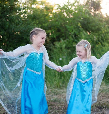 Two girls holding hands outdoors wearing Ice Queen Dress with Cape Size 3-4 in peacock blue satin and crystal organza sleeves.