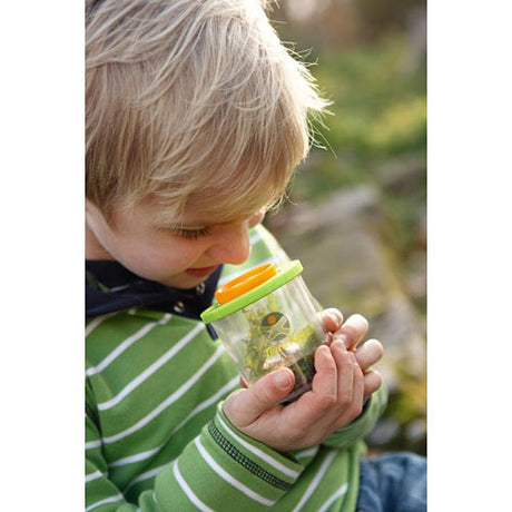 Child exploring outdoors with Terra Kids | Beaker Bug Magnifier observing a plastic spider inside the jar.