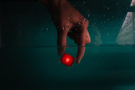 Hand placing a glowing red cube with a smiley face underwater, showcasing Glo Pals Red light-up toy.