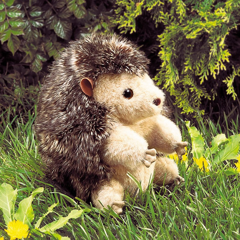 Hedgehog Puppet with soft plush face, fluffy back, and movable fingers, sitting in grass surrounded by greenery.