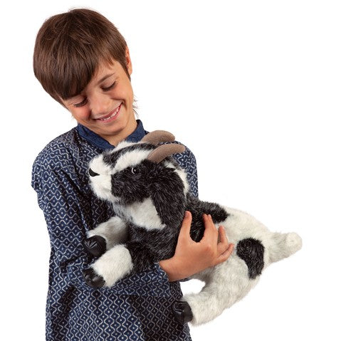 Child happily holding a soft, salt-and-pepper Goat Puppet with floppy ears and stuffed horns.