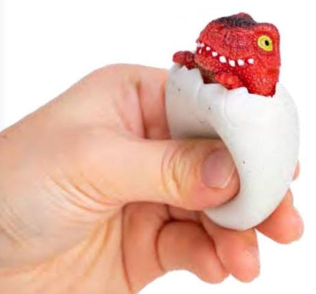 Hand squeezing a Squeezy Peek Hatcher Dino toy with a red dinosaur popping out of a white egg shell.