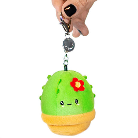 Hand holding a green Cactus Micro plush keychain with a red flower and smiling face, soft and adorable design.
